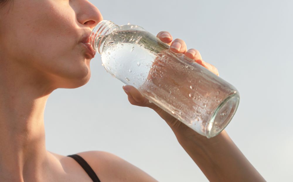 donna che beve acqua fresca dalla bottiglia per contrastare la sudorazione intensa alle mani